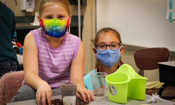 Two girls smile while making a fossil in a cup